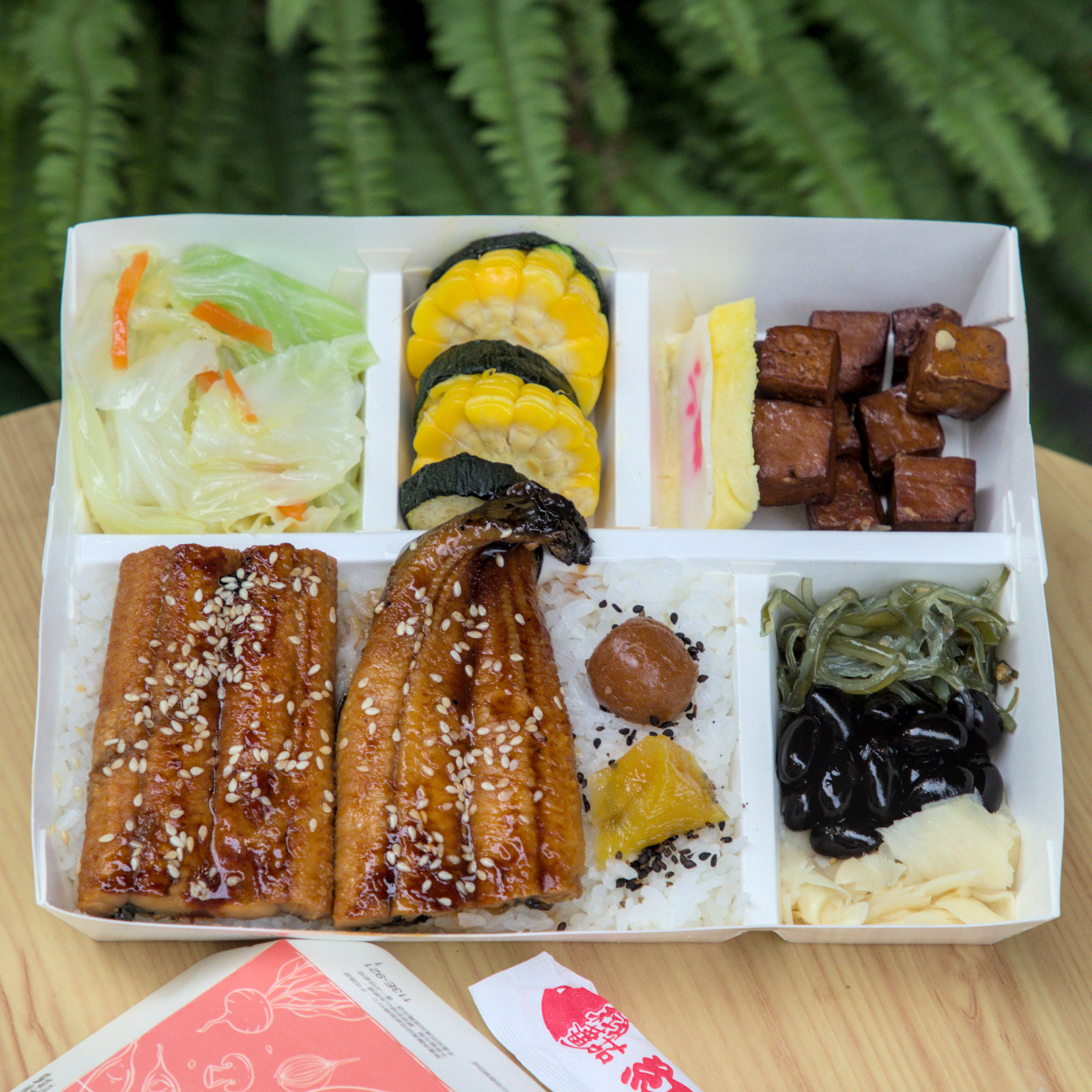 紅蕃茄330元鰻魚飯,豐盛的日式鰻魚便當 紅蕃茄330元鰻魚飯全景,便當裡有兩大片蒲燒鰻魚,搭配清炒高麗菜、蜜汁豆干、玉子燒等豐富配菜,色彩豐富,擺盤精緻,是視覺與味覺的雙重饗宴。