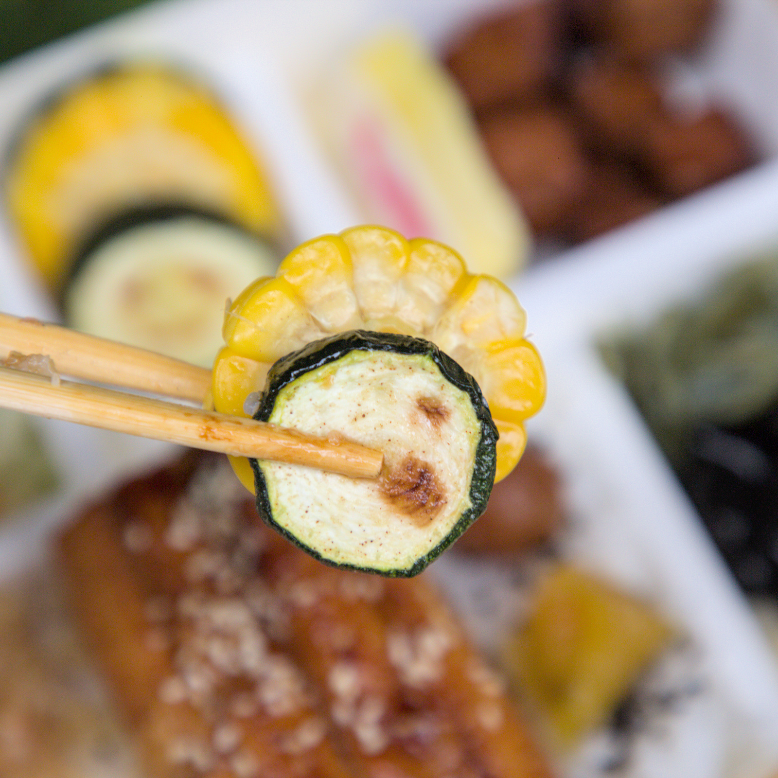 紅蕃茄鰻魚飯,健康美味的烤玉米與烤櫛瓜 紅蕃茄鰻魚飯的配菜特寫,包含烤玉米與烤櫛瓜,展現便當的多元配菜組合,確保營養均衡,口感豐富。