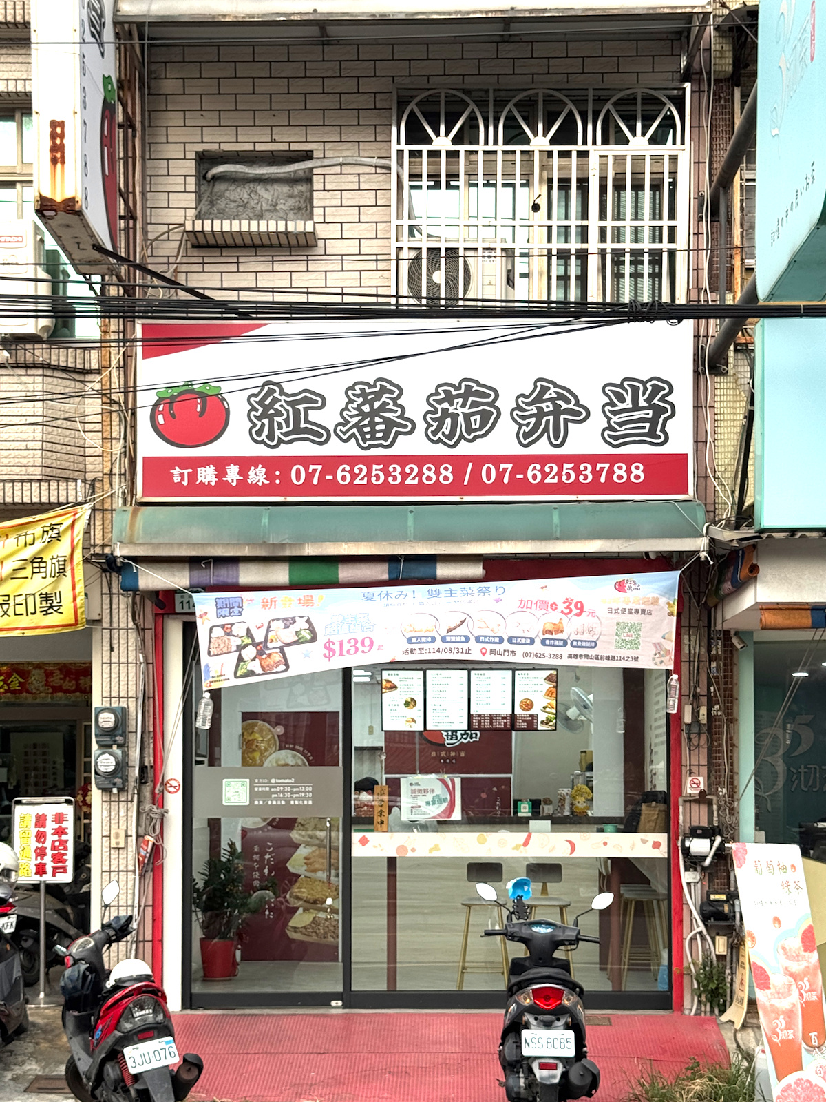 高雄岡山紅蕃茄日式便當專賣店外觀,顯眼紅色招牌,兩層樓建築 紅蕃茄日式便當專賣店的店面外觀,簡約明亮的兩層樓建築,搭配顯眼的紅色招牌與大片玻璃門,方便顧客一眼辨識。門口停著幾台機車,顯示出這家店的高人氣與外帶便利性。